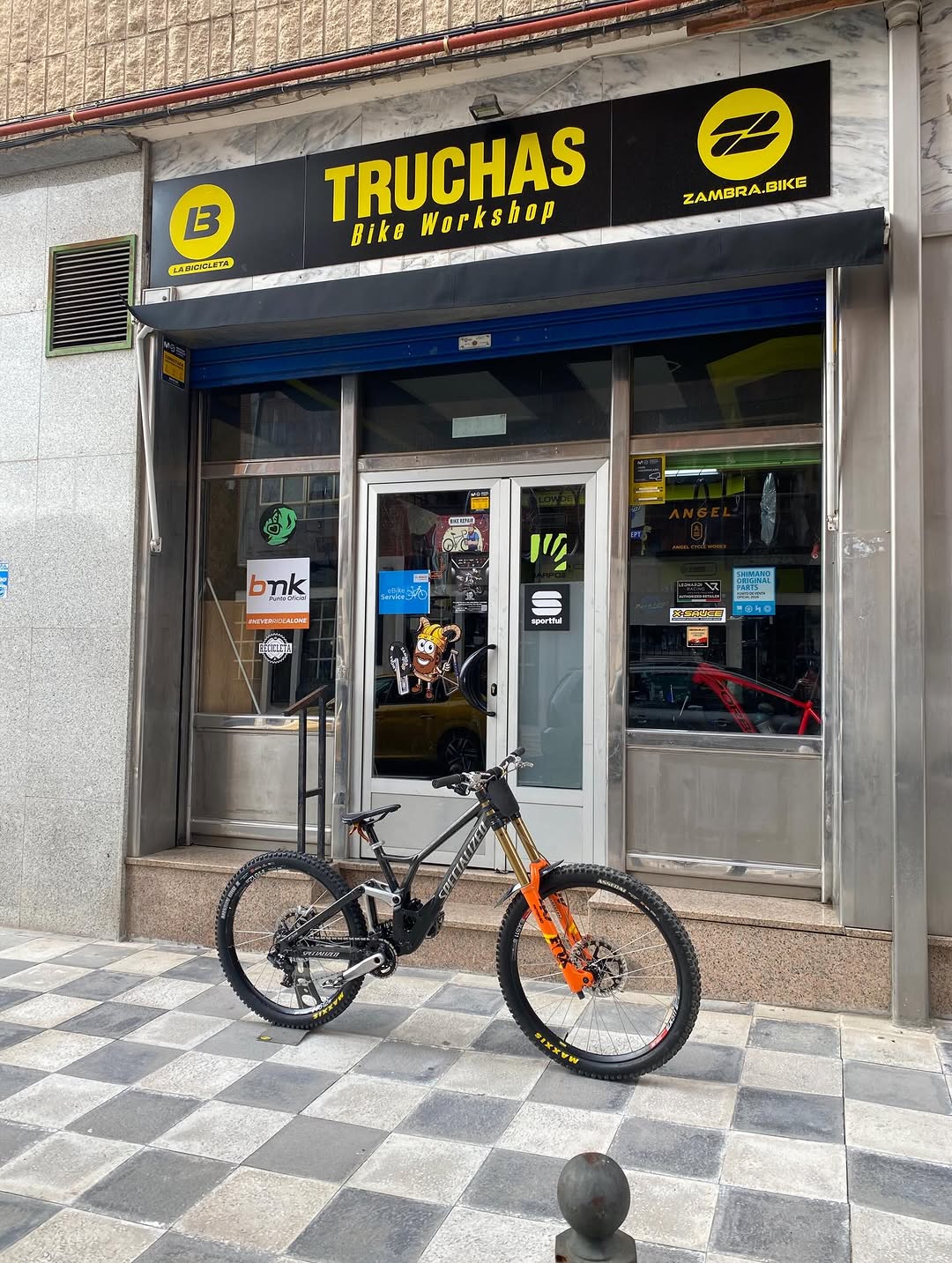 Fachada de Truchas Bike Workshop con una bici de descenso aparcada